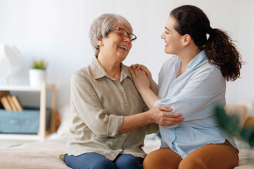 Beautiful mother and daughter are talking and smiling while sitting on bed at home